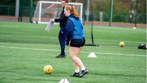 Female student on football pitch kicking ball