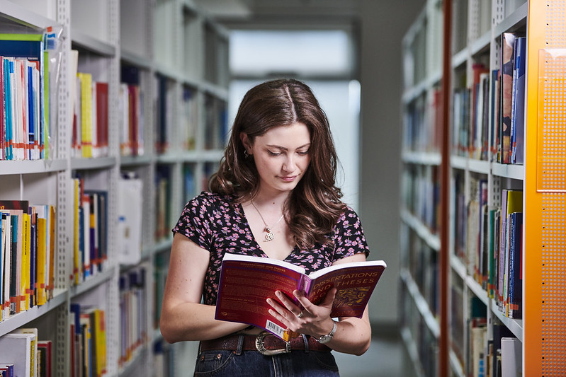 student reading a text book in the library aisles