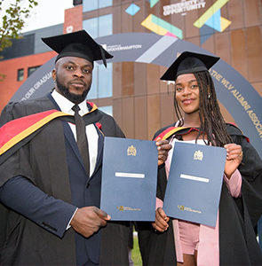 Two students proudly holding their degree certificates while wearing their cap and gowns.