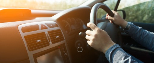 Hands on the steering wheel of a car, driving under evening sunlight