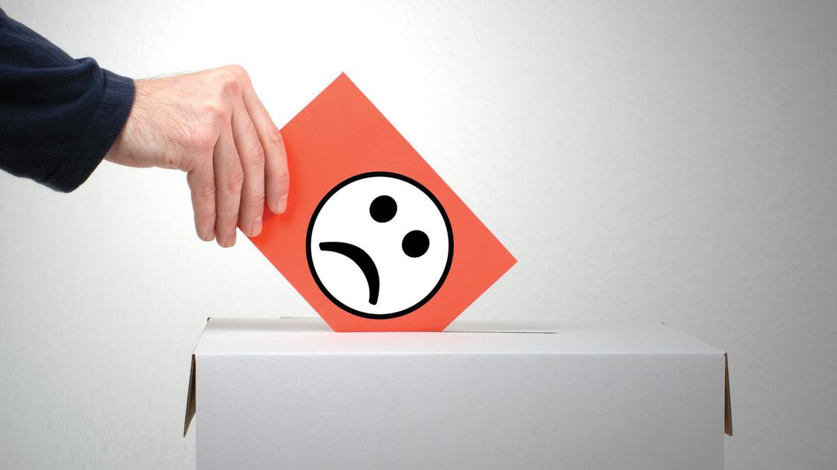 A hand placing an orange sheet of paper with a graphic of a sad face into a box.