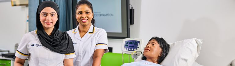 Two nursing students standing over dummy and smiling