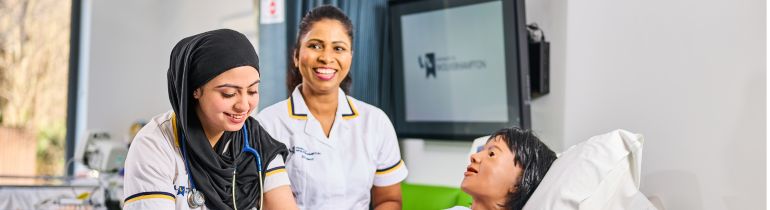 Two Nursing students standing next to dummy and smiling at camera