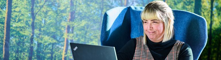 A female student sitting on chair in Education building working on laptop