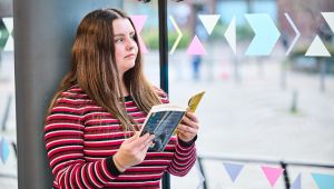 Female student looking out of window with book in her hands