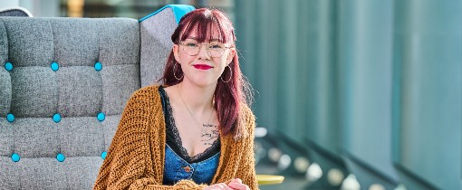 Person sitting on a modern gray chair with turquoise buttons, wearing a chunky brown knitted cardigan.