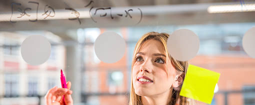 Student stood looking at glass that has post it notes on as well as marker pen writing.