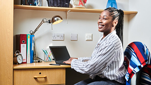Student sat at desk working on laptop and smiling