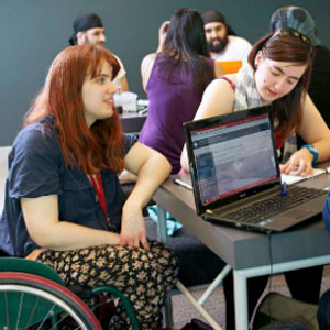 image of group of people sitting around laptop one in a wheelchair
