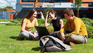Photograph of three students sitting on the grass in the Wolverhampton City Campus courtyard.