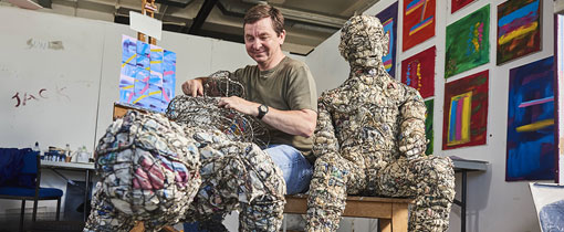 Student working on an art piece where humanoid metal frameworks are filled with various papers to give them form