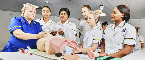Students in nursing uniforms observing a demonstration on a mock patient