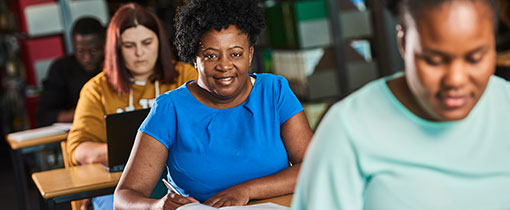 Mature students sitting at desks in a classroom, one looking towards the camera and smiling
